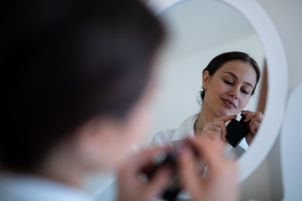 一位女性在照镜子时喷洒香水，体现自我呵护。素材图片图片下载