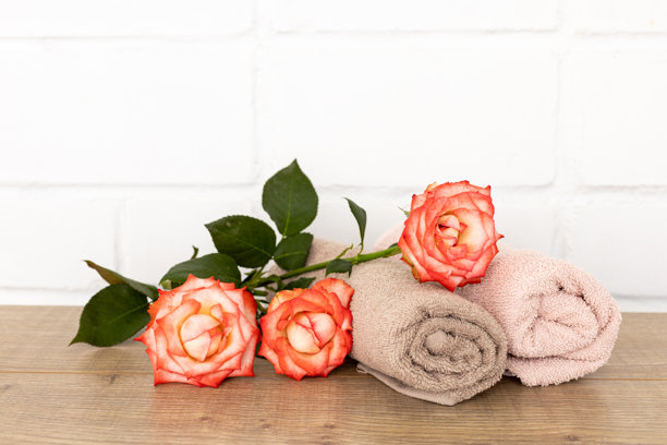 木板上堆叠着柔软的毛巾，旁边放着玫瑰花图片下载