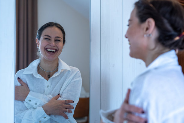 女子对着镜子里的自己微笑大笑。素材图片图片下载