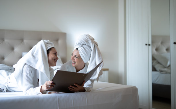 穿着浴袍的快乐年轻女性朋友在床上放松。图片素材图片下载