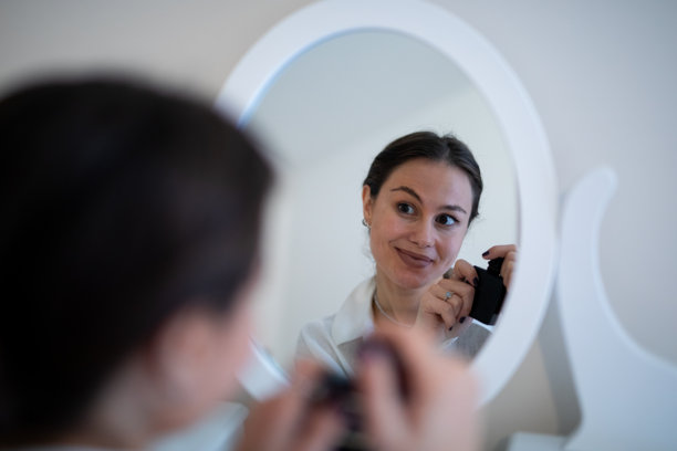 一位女士对着镜子微笑，正在化妆打扮。素材图片图片下载