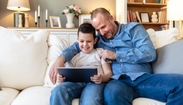 平板电脑，放松，父子俩在家客厅沙发上玩在线视频游戏。在起居室里，快乐的父子俩通过数字技术一起玩电子竞技，爸爸教儿子玩游戏，享受亲子时光。图片下载
