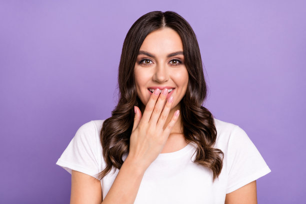 身穿白色T恤的有趣棕发千禧年女士，在紫色背景下大笑的特写照片图片下载