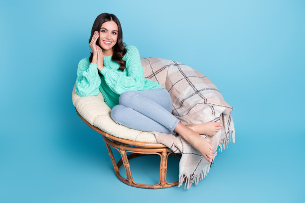 一名疲倦的金发年轻女子穿着毛衣和牛仔裤，独自坐在蓝色背景前，全景照片图片下载