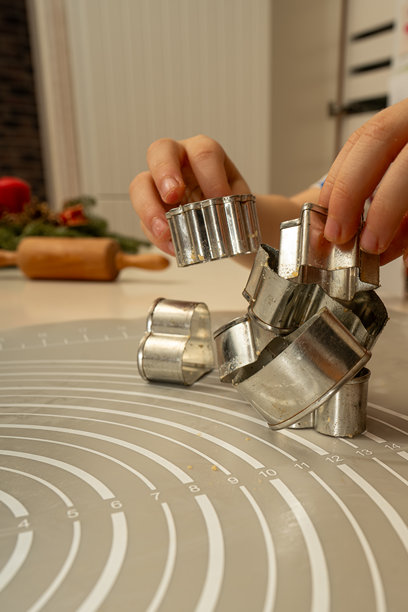 孩子在厨房的桌子上玩耍，用金属饼干模具搭建塔。背景是擀面杖和节日装饰。图片下载