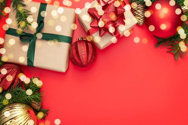圣诞装饰，由杉树枝、松果、红色球体、礼品盒组成，用牛皮纸包装，饰以绿红丝带，背景为红色。圣诞快乐，新年快乐。贺卡。留白。图片下载