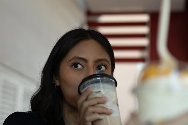 一位年轻女子在现代咖啡馆里享用清爽的珍珠奶茶，侧目而视，眼神好奇，轻轻啜饮，展现出放松的惬意和淡淡的微笑。图片下载