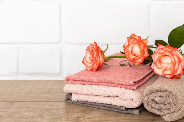 木板上堆叠着柔软的毛巾，旁边点缀着玫瑰花图片下载