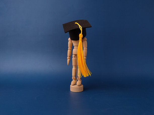 图片展示了一个木制艺术家模特，戴着迷你毕业帽和黄色流苏，背景为蓝色。图片下载