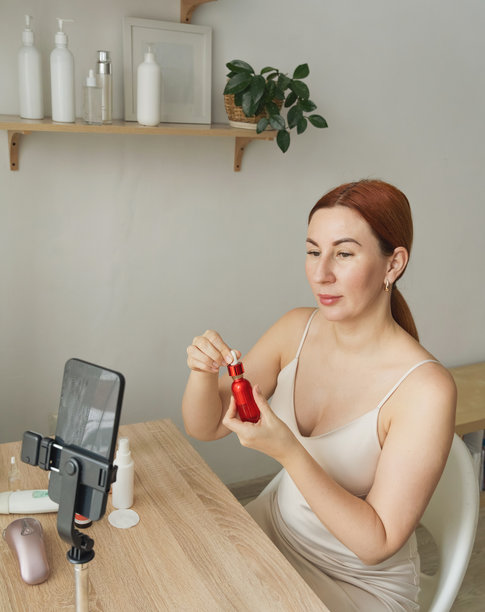 一位女性正在创作美妆内容，对着镜头进行关于护肤精华的视频博客。一位受欢迎的社交媒体美妆博主正在录制教学视频，并在她的频道上进行产品评测。图片下载