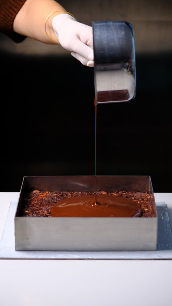 厨师将液态巧克力甘纳许倒入厨房桌上的方形蛋糕模具框架中图片下载