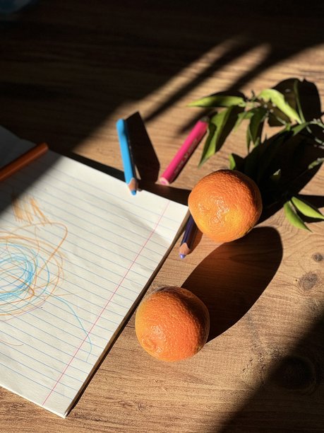 木桌上，阳光戏剧性地静置着新鲜的橘子、儿童涂鸦和彩笔。图片下载