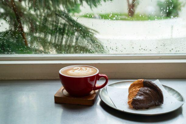 热咖啡拿铁，咖啡拉花奶泡，杯子里的天鹅形状，搭配巧克力可颂，摆放在木质桌面上，俯视角度。作为咖啡店或咖啡馆的早餐，适合工作时段，雨季概念。图片下载