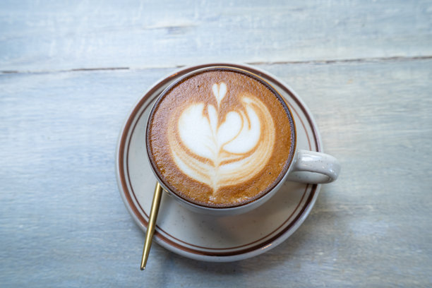 俯视角度，木桌上放着一杯带有拉花奶泡的热咖啡拿铁，作为咖啡店的早餐，适合工作时的咖啡馆，复古风格。图片下载
