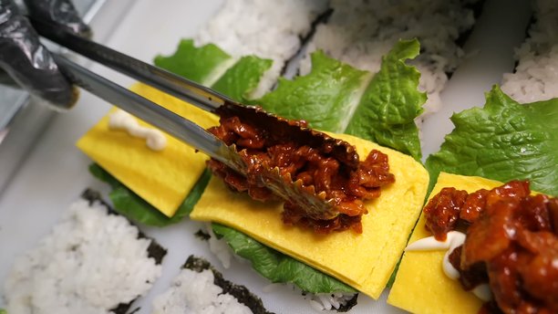 用夹子将辣肉放在鸡蛋和米饭卷上图片下载