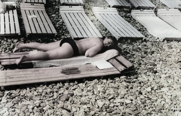 一位中年女子躺在木制沙滩躺椅上晒太阳的复古肖像。她享受着阳光和温暖。摄于1971年的老照片。图片下载