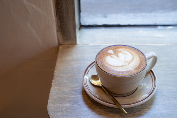 咖啡店里，一张摆在木桌上的热咖啡拿铁，上面有拉花奶泡，俯视角度。作为早餐，在咖啡馆，适用于商务工作场景，复古风格。图片下载