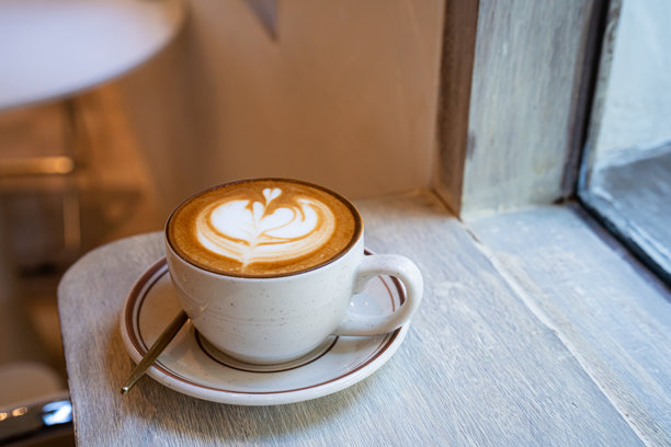 俯视角度，木桌上的咖啡杯中盛有热拿铁咖啡，带有拉花奶泡，作为咖啡店的早餐，适用于工作场景，复古风格。图片下载