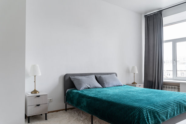 宽敞明亮的卧室，配有双人床。床上铺着绿色的床罩和枕头。卧室照片，光线不同。房间里有一个大大的白色衣柜。图片下载