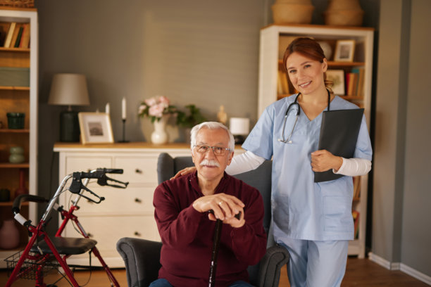 护士手持写字板，正在搀扶一位坐在扶手椅里的老人图片下载
