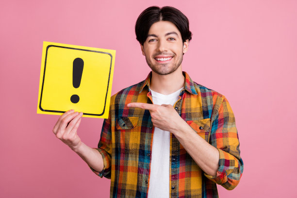照片：迷人的可爱年轻绅士穿着格子服装，手指指向带有感叹号的告示牌，背景为粉红色图片下载
