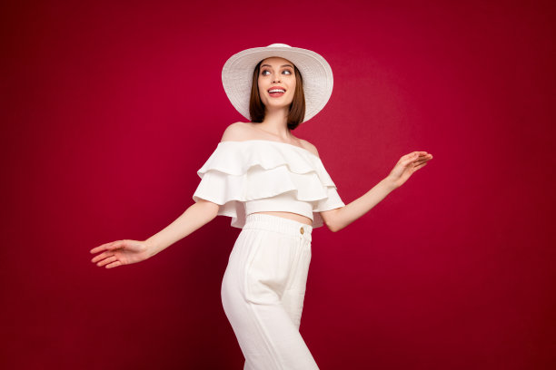 照片：可爱的棕色千禧一代女士，戴着帽子，穿着露肩衬衫和裤子，孤立在红色背景上，目光望向远方。图片下载