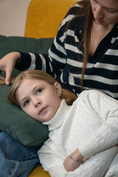 母亲在舒适的沙发上温柔地抚摸着年幼女儿的头发，在家中分享着平静的亲情和家庭的羁绊。竖式照片图片下载
