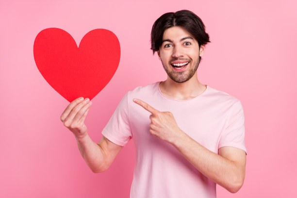 照片中的男人竖起手指，指向一张纸制的心形明信片，背景是孤立的粉彩色调图片下载