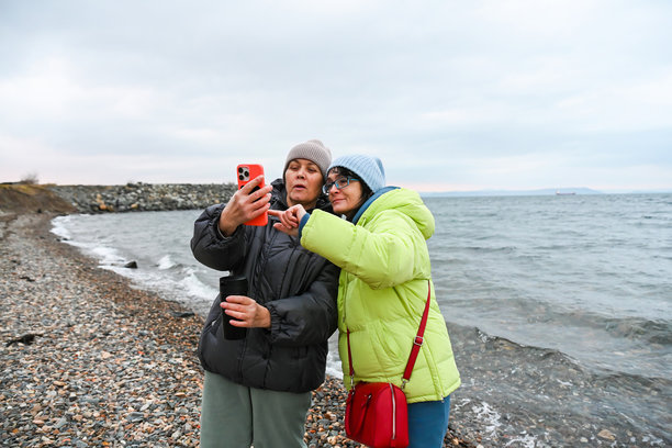 两位分别50岁和60岁的俄罗斯朋友在春日的海边散步，一同回顾照片，分享指导、支持和有意识的学习，享受宁静的时刻。图片下载