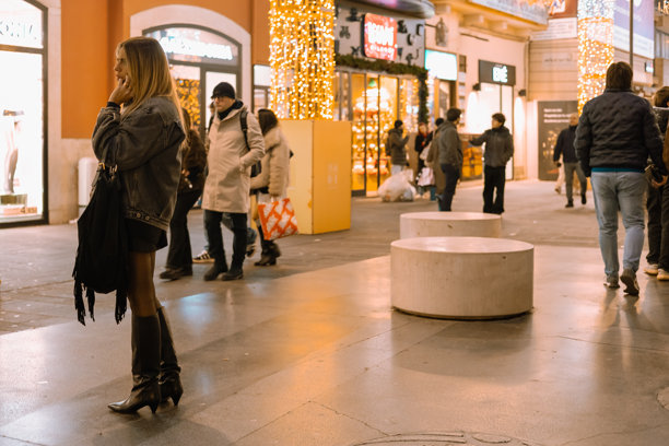 意大利巴里，一位时尚年轻女子夜间走在繁华的商业街，周围是灯火辉煌的店面和圣诞节的节日装饰。图片下载