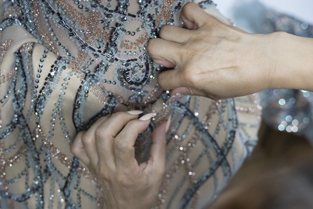 一位裁缝的手正在缝制一件奶油色和蓝色的珠饰晚礼服。素材图片图片下载