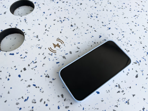 智能手机放在有斑点的桌子上，旁边是无线充电符号。现代化的车载技术，旨在公共交通中提供便利和数字连接。图片下载