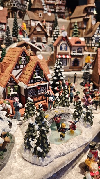 舒适的迷你圣诞村庄，有被雪覆盖的房屋、松树和在冰冻池塘上滑冰的人们。该图片代表了节日传统、怀旧、冬季庆祝和节日气氛。图片下载