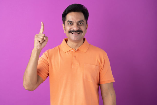 印度中年男子身穿橙色T恤，孤立在紫色背景上的照片素材图片下载