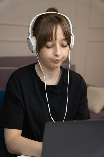 年轻女子戴着耳机，坐在舒适客厅的白色桌子前，用笔记本电脑工作。享受属于自己的空间里的音乐。竖幅照片图片下载