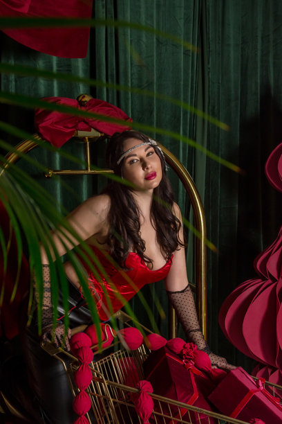 一位年轻美丽的女子，身着手套和复古风格的发带装饰，站在一辆装满礼物的购物车旁。图片下载