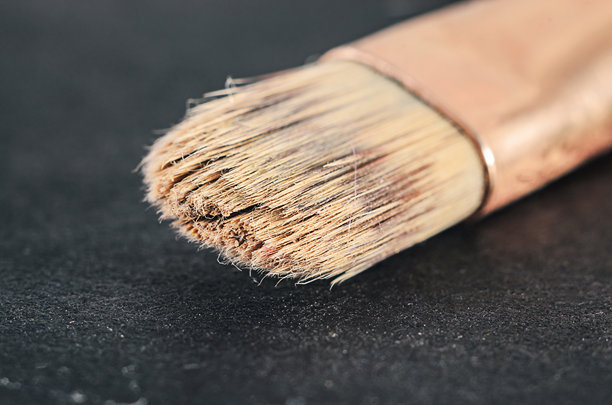 特写镜头，画面为黑色背景上一支旧的、用过的画笔，展示了磨损的木柄、散开的刷毛以及先前绘画的痕迹，非常适合艺术、创意和艺术概念插画。图片下载