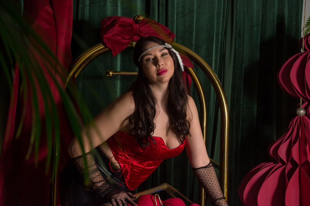 一位年轻美丽的女子，身着手套和复古风格的发带装饰，站在酒店室内的一个行李车旁。图片下载