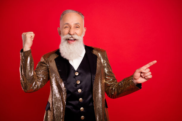 照片：一位穿着金色夹克的滑稽灰胡子老人表演者，指向空白处，背景是纯红色图片下载