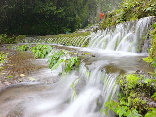 一个风景如画的瀑布穿过覆盖着苔藓的石拱，在充满活力的绿色植物中形成了一个雾气缭绕、宁静的水景。这是自然、旅行和户外生活主题的理想图片。图片下载