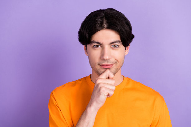 照片：一位年轻、快乐、迷人的男士，手托下巴，若有所思，聪明地站在紫色背景前图片下载