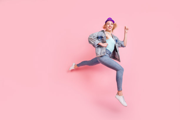 穿着牛仔夹克、戴着遮阳帽的印象深刻的金发千禧年女士的全身侧面照片，她穿着运动服，孤立在粉色背景上图片下载