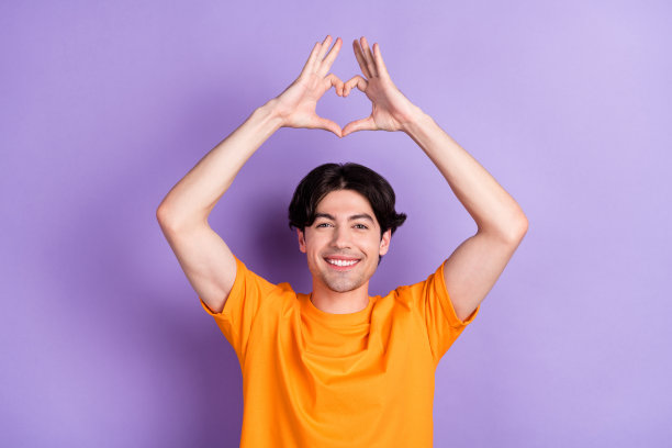照片：一个快乐迷人的男人，头上比出小爱心手势，孤立在紫色背景上图片下载