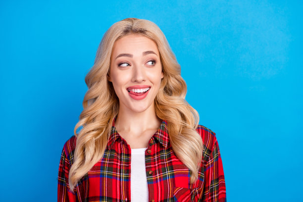 照片：漂亮的金色头发千禧一代女士伸出舌头，望向远方，身穿红色衬衫，背景为蓝色。图片下载