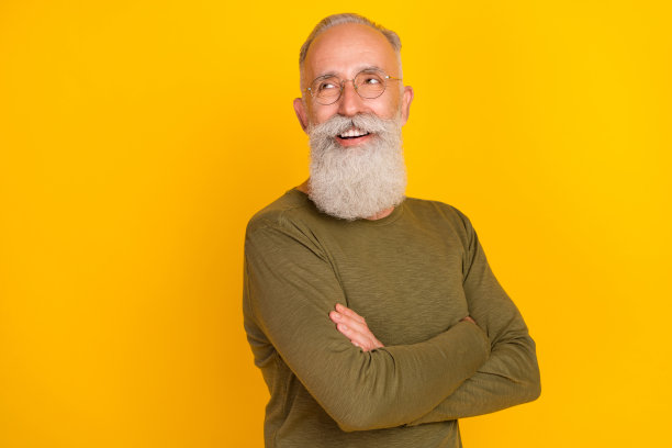 照片：一位穿着绿色衬衫、戴着眼镜、双臂交叉、目光望向虚空的创意自信老人，背景为黄色。图片下载