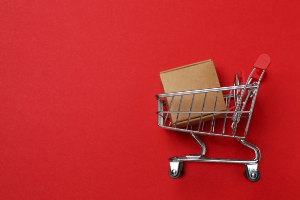 红色表面上带有纸板箱的小型购物车特写照片。购物概念。图片下载