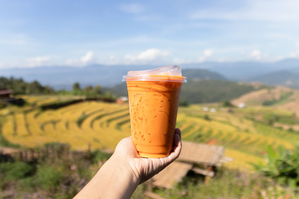 冰镇奶茶配绵密泡沫，背景为层叠的梯田风光，阳光明媚温暖，氛围悠闲图片下载