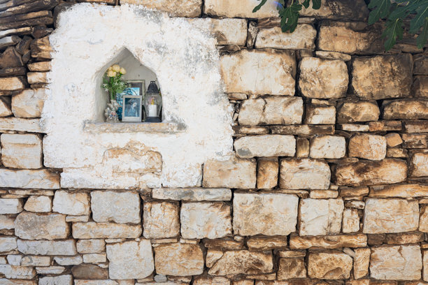 质朴的石墙圣龛，内有圣徒照片、鲜花和壁龛，位于简陋的户外墙上图片下载