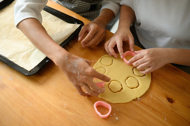 特写和俯视拍摄，一对情侣的手在家庭厨房的木桌上将饼干模具按入擀好的面团中图片下载