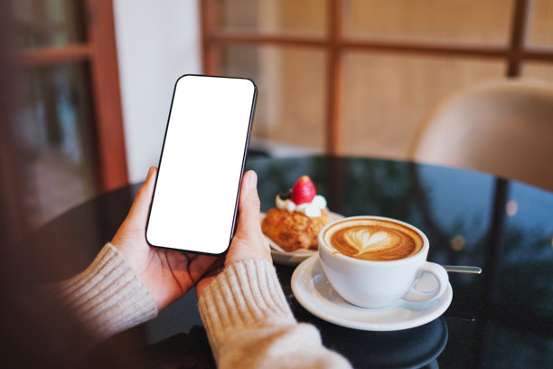 咖啡馆里，一名女子正手持并使用着手机，背景是空白的桌面屏幕的样机图图片下载